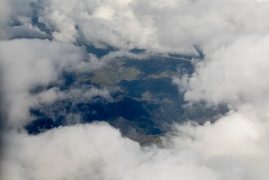 Vista aérea de montanhas parcialmente encobertas por nuvens densas, revelando picos e vales.