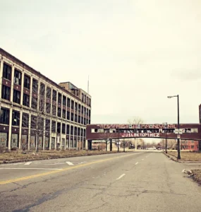 Vista de uma rua deserta cercada por prédios industriais abandonados em Detroit, com janelas quebradas e grafites nas paredes