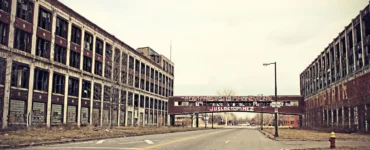 Vista de uma rua deserta cercada por prédios industriais abandonados em Detroit, com janelas quebradas e grafites nas paredes