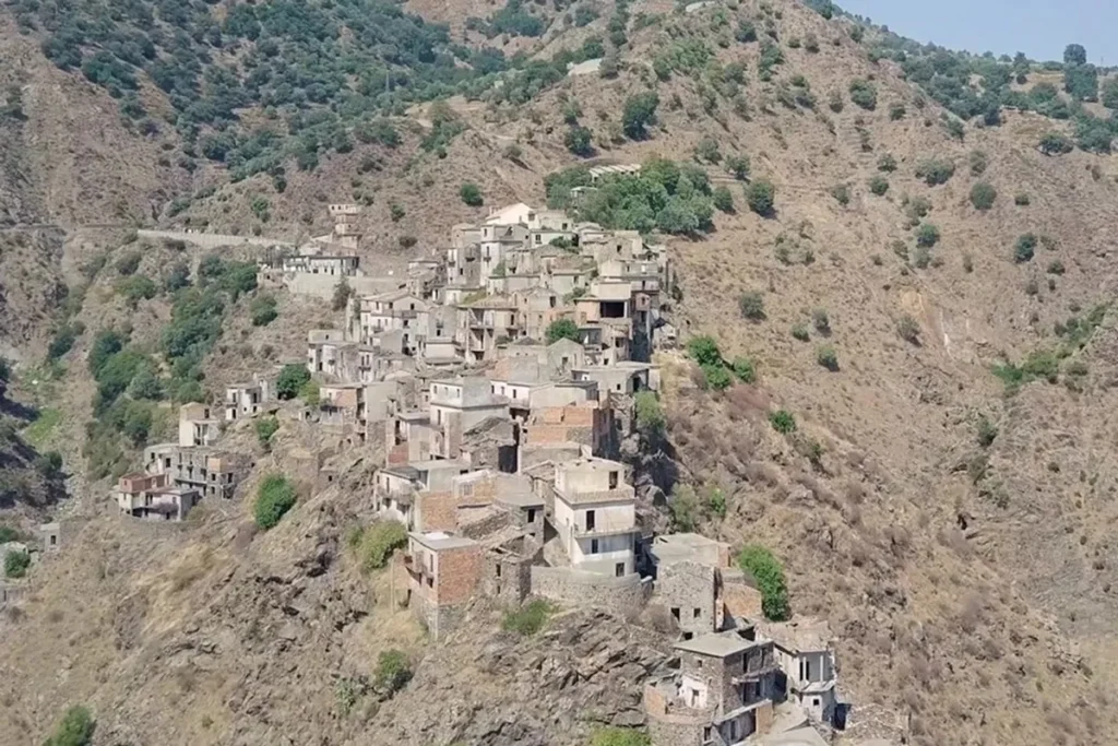 Vista aérea de uma cidade fantasma construída em encosta rochosa, com casas de pedra e tijolos abandonadas entre montanhas áridas