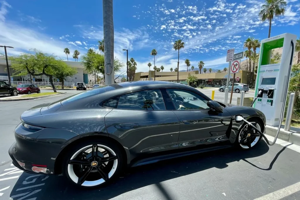 Porsche Taycan preto conectado a estação de carregamento elétrico em área urbana, simbolizando mobilidade sustentável e inovação automotiva