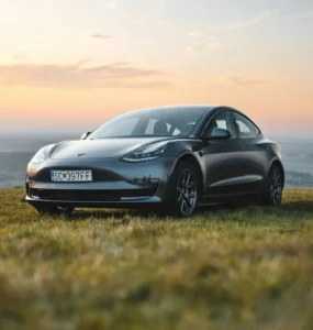 Tesla Model 3 preto estacionado em campo aberto durante o pôr do sol, simbolizando inovação, sustentabilidade e mobilidade elétrica