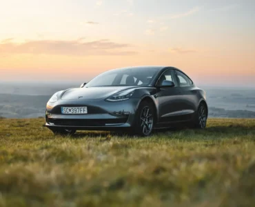 Tesla Model 3 preto estacionado em campo aberto durante o pôr do sol, simbolizando inovação, sustentabilidade e mobilidade elétrica