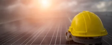 Capacete de segurança amarelo sobre painéis solares com sol ao fundo, simbolizando energia solar sustentável, inovação e segurança no trabalho.