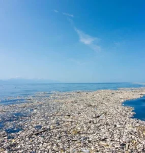 Imagem de uma imensa mancha de poluição plástica no oceano, conhecida como ilha de lixo, mostrando garrafas, embalagens e detritos acumulados na superfície da água sob um céu azul.