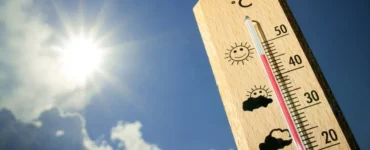 Termômetro de madeira marca temperatura próxima a 40 °C sob sol forte em céu azul, simbolizando onda de calor.