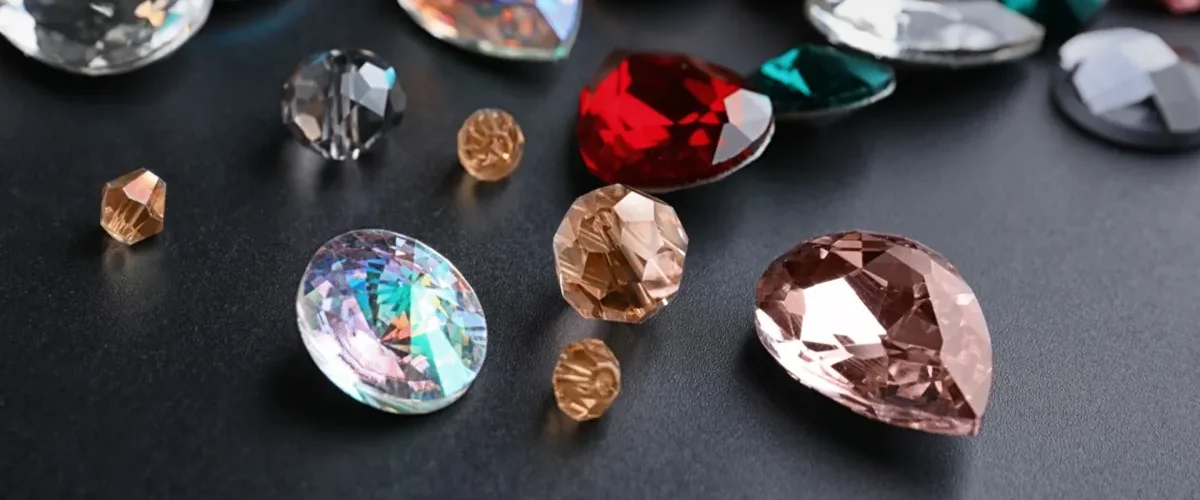 Diversas pedras preciosas lapidadas em cores vibrantes como vermelho, azul, rosa e dourado sobre fundo preto