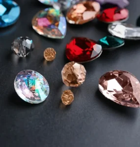 Diversas pedras preciosas lapidadas em cores vibrantes como vermelho, azul, rosa e dourado sobre fundo preto