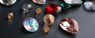 Diversas pedras preciosas lapidadas em cores vibrantes como vermelho, azul, rosa e dourado sobre fundo preto