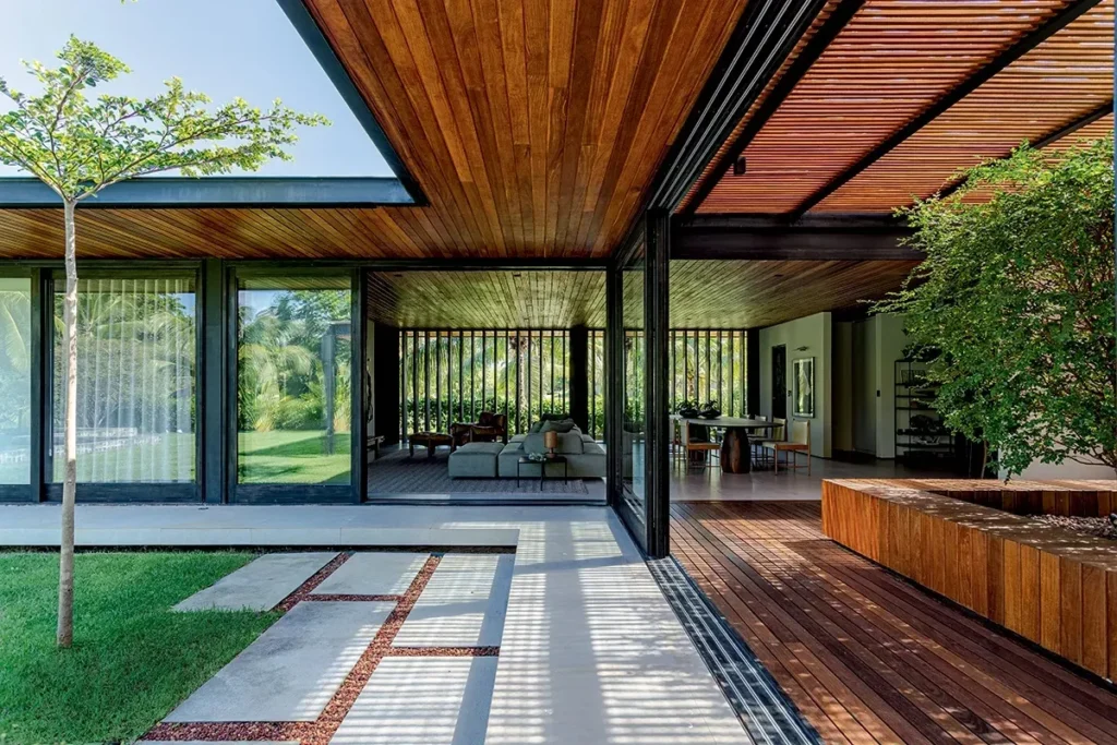 Fachada interna de casa moderna com teto de madeira, grandes portas de vidro, jardim integrado e ventilação cruzada que conecta sala de estar, varanda e área verde.