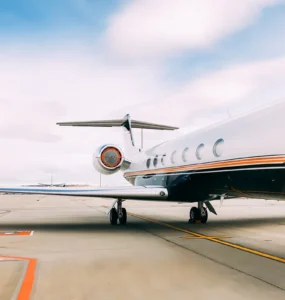 Jato executivo branco e preto estacionado em uma pista de aeroporto, com céu parcialmente nublado e tons suaves de azul e branco ao fundo.