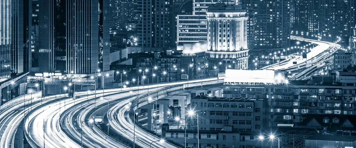 Vista noturna de uma cidade inteligente com arranha-céus iluminados e rodovias elevadas cheias de luzes de tráfego em movimento.