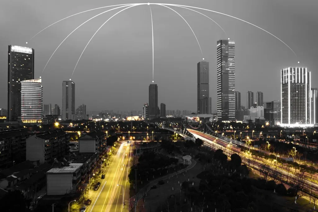 Panorama noturno de uma cidade inteligente com arranha-céus iluminados e linhas de conexão digital representando tecnologia e conectividade urbana.