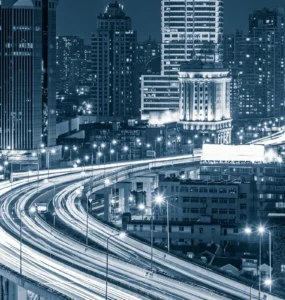 Vista noturna de uma cidade inteligente com arranha-céus iluminados e rodovias elevadas cheias de luzes de tráfego em movimento.