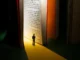 Miniatura de pessoa observando um livro gigante iluminado, representando a busca pelo conhecimento e a importância da divulgação científica.