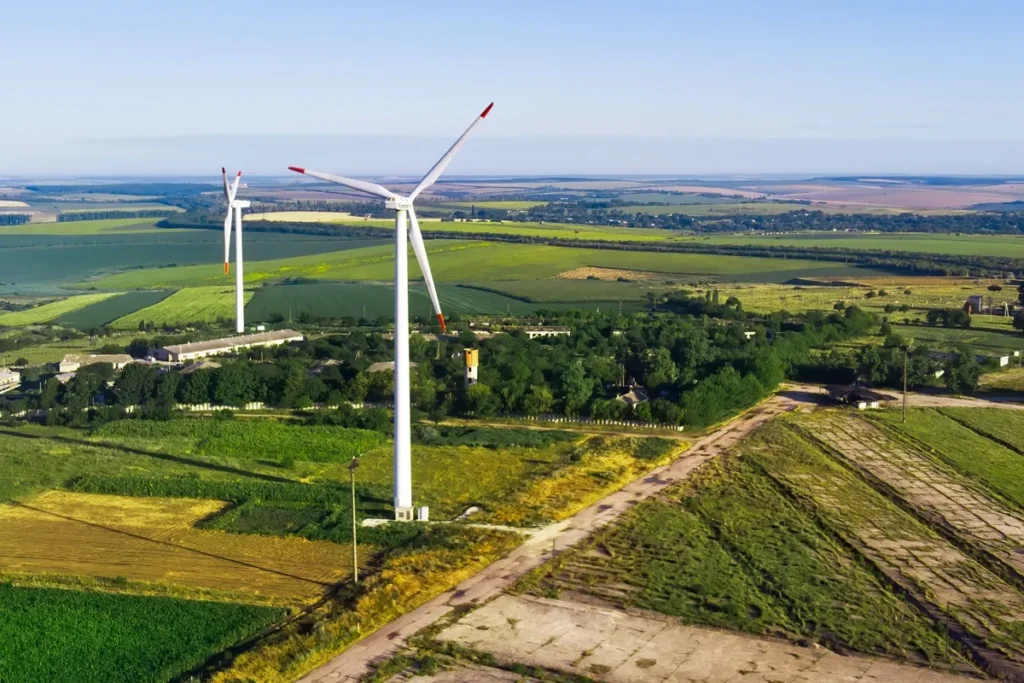 Vista aérea de turbinas eólicas em meio a plantações verdes, simbolizando o uso de energia limpa e sustentável no campo.