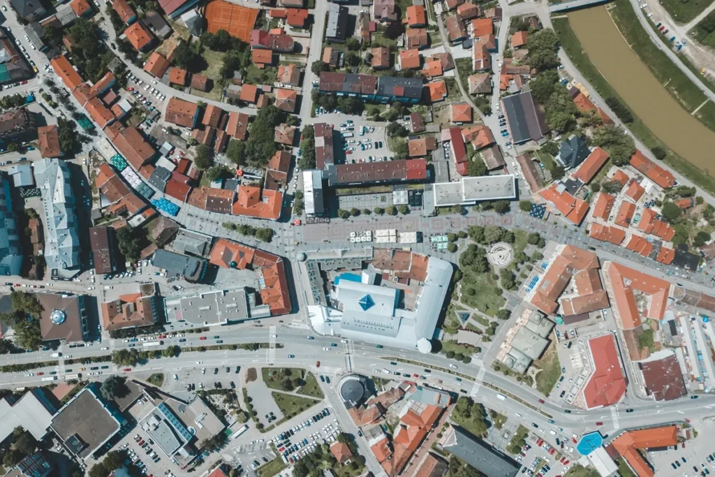 Imagem aérea de uma cidade europeia com ruas sinuosas, construções de telhados vermelhos e áreas verdes, destacando o planejamento urbano e a arquitetura tradicional.