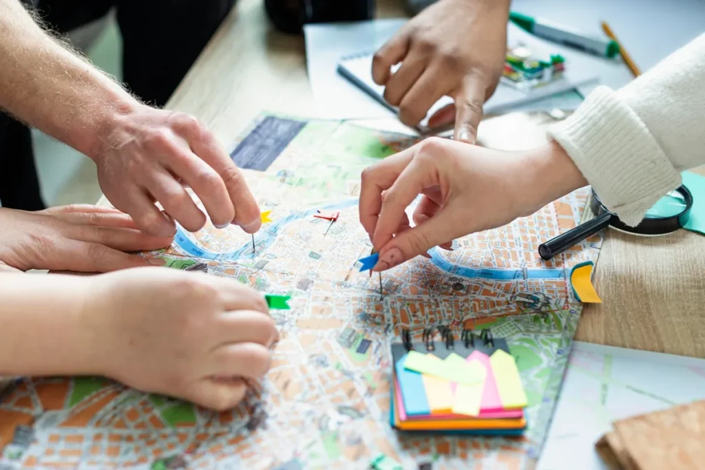 Mãos posicionando alfinetes coloridos em um mapa de cidade, representando planejamento urbano, estudo geográfico e análise de território.