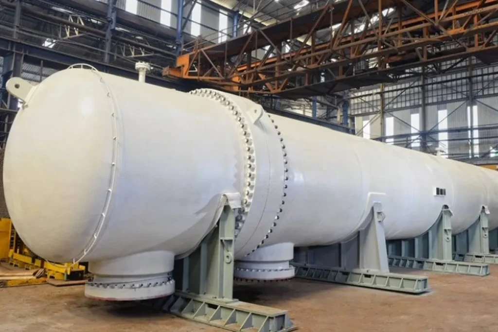 Grande trocador de calor cilíndrico branco instalado em uma planta industrial, com estrutura metálica de suporte e tubulações em ambiente fabril iluminado.