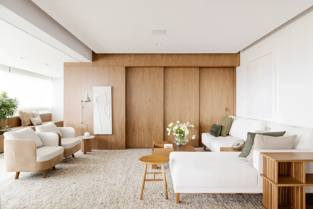 Sala de estar com decoração minimalista e design contemporâneo, destacando móveis em madeira clara, sofá branco e poltronas bege sob iluminação natural suave.