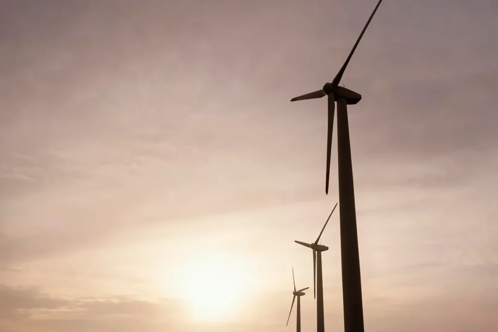 Três turbinas eólicas em operação sob o céu alaranjado do entardecer, representando a geração de energia limpa e sustentável.