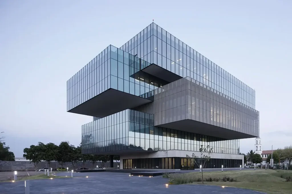 Prédio corporativo contemporâneo com estrutura geométrica de volumes sobrepostos e fachadas de vidro espelhado refletindo o céu.