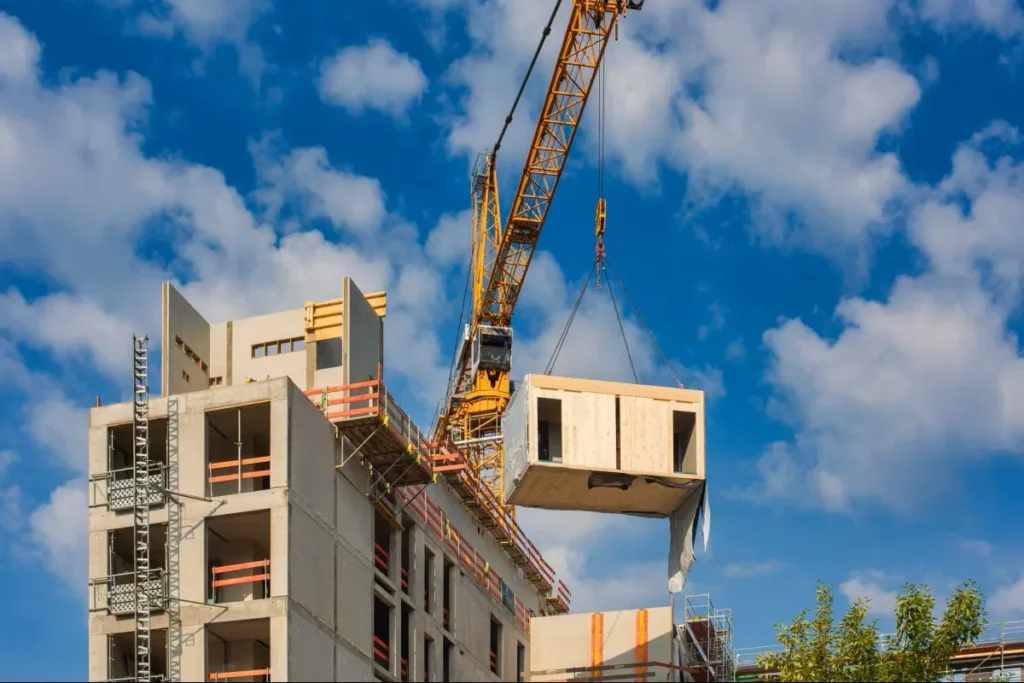 Guindaste ergue e instala módulo pré-fabricado de madeira em edifício em construção, com estrutura de concreto e andaimes ao redor.