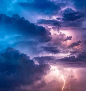 Nuvens densas iluminadas por relâmpagos durante uma tempestade elétrica, com tons de azul e roxo no céu, representando fenômenos meteorológicos intensos.
