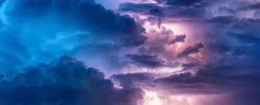 Nuvens densas iluminadas por relâmpagos durante uma tempestade elétrica, com tons de azul e roxo no céu, representando fenômenos meteorológicos intensos.