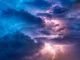 Nuvens densas iluminadas por relâmpagos durante uma tempestade elétrica, com tons de azul e roxo no céu, representando fenômenos meteorológicos intensos.