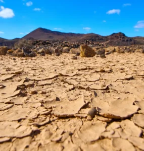 Solo rachado e árido sob um céu azul em região desértica, representando os efeitos da desertificação e escassez de água.