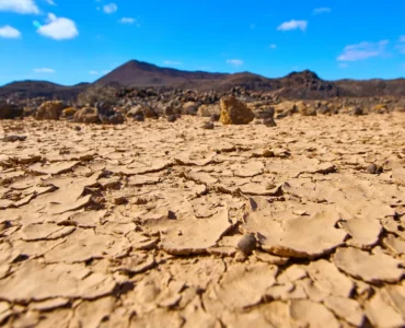 Solo rachado e árido sob um céu azul em região desértica, representando os efeitos da desertificação e escassez de água.