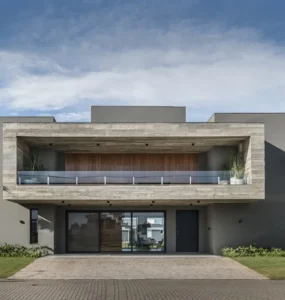 Fachada de casa moderna em estilo brutalista com estrutura de concreto aparente, linhas retas, grandes aberturas de vidro e paisagismo com palmeiras.