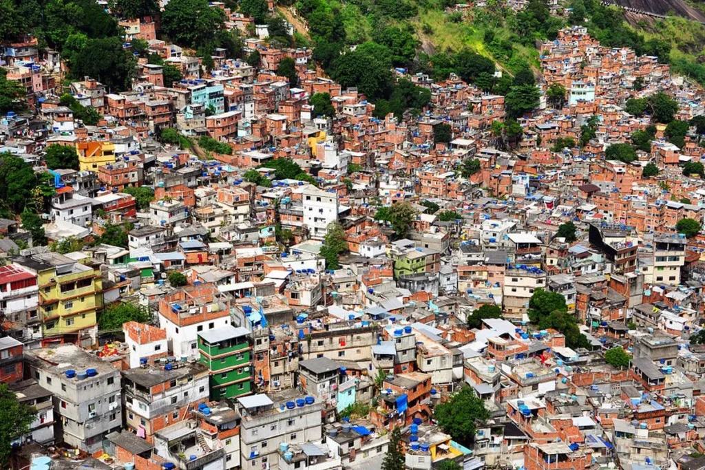 Vista panorâmica de uma favela construída em área de morro, com casas coloridas, ruas estreitas e vegetação entre as edificações.