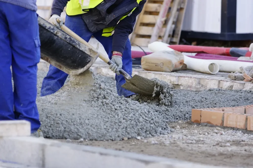 Trabalhadores despejando e nivelando concreto fresco com pá em uma obra de construção civil.