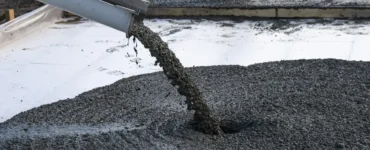 Concreto usinado sendo despejado por calha sobre base de obra, com trabalhador nivelando o material ao fundo.