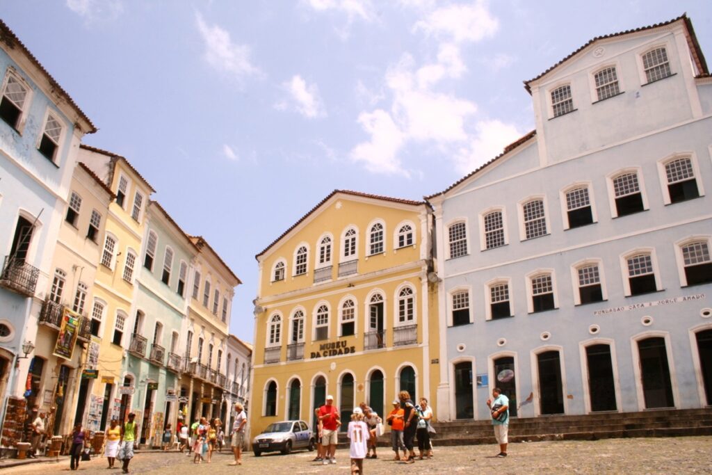 Prédios coloniais coloridos do Pelourinho, em Salvador, com turistas caminhando por rua histórica em dia ensolarado.