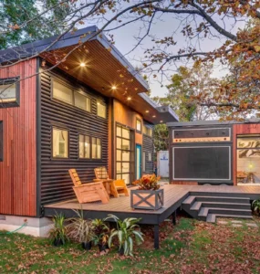 Tiny house moderna com fachada de madeira e metal, deck amplo com poltronas, iluminação embutida e miniestúdio anexo com design que imita um amplificador.