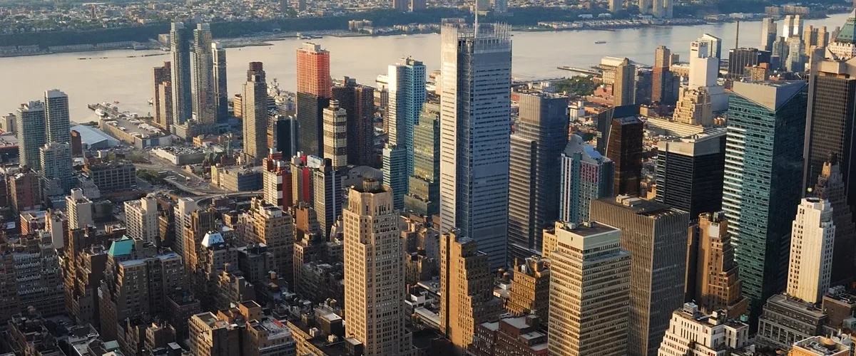 Panorama aéreo de Manhattan em Nova York, com arranha-céus iluminados pelo pôr do sol e o rio Hudson ao fundo.