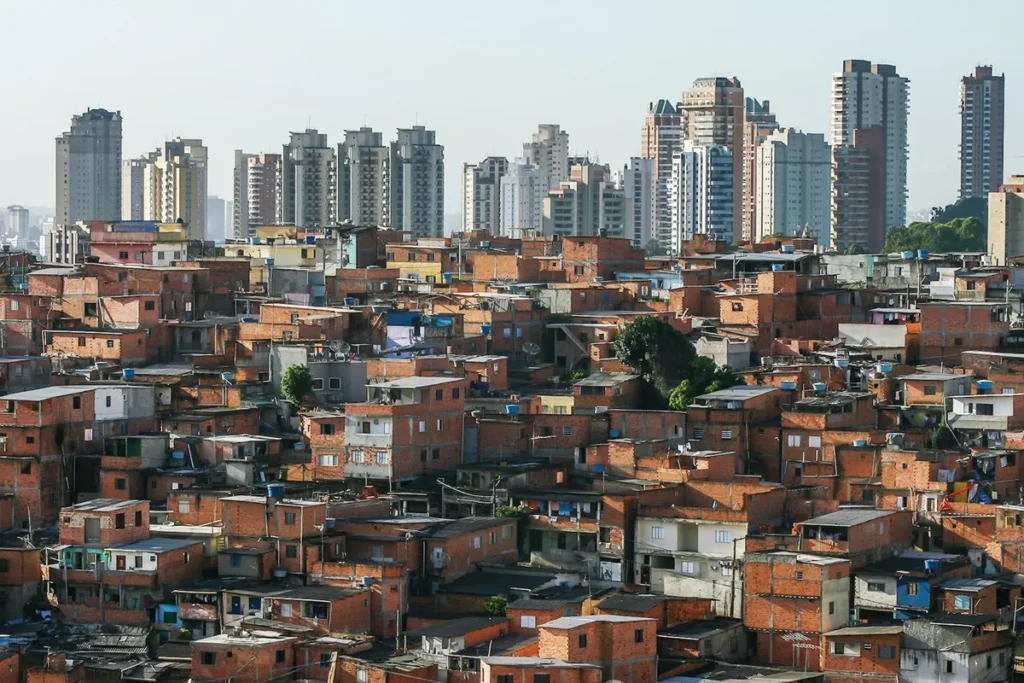 Vista panorâmica de uma comunidade com casas de tijolo aparente em contraste com prédios altos e modernos ao fundo.