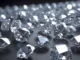 Diamantes lapidados com facetas brilhantes dispostos sobre superfície escura, refletindo luz e destacando o alto grau de transparência.