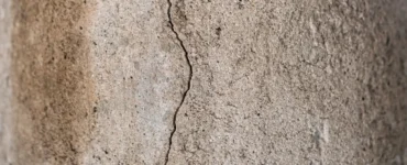 Rachadura vertical em parede de concreto mostrando desgaste e pequenos desprendimentos na superfície.