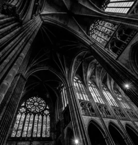Interior de catedral gótica com colunas altas, arcos ogivais e vitrais iluminados, fotografado em preto e branco.