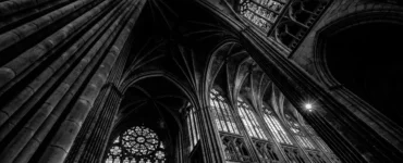 Interior de catedral gótica com colunas altas, arcos ogivais e vitrais iluminados, fotografado em preto e branco.