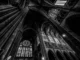 Interior de catedral gótica com colunas altas, arcos ogivais e vitrais iluminados, fotografado em preto e branco.
