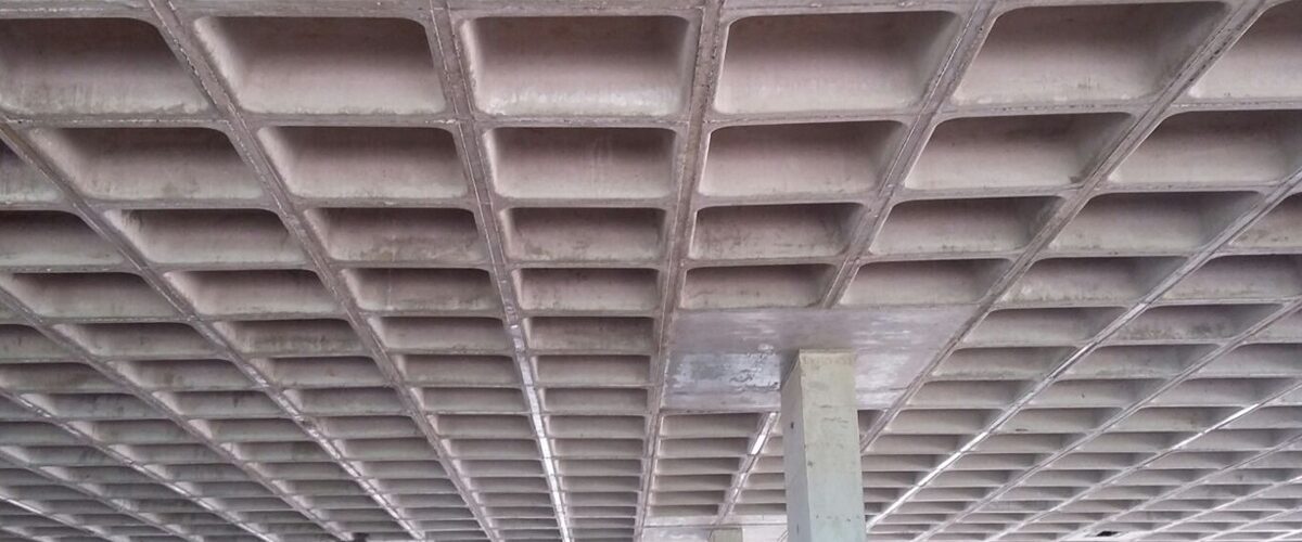 Vista inferior de laje nervurada em concreto armado, com nervuras aparentes apoiadas em pilares estruturais.