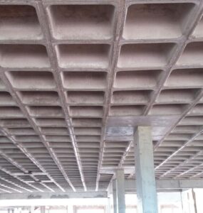 Vista inferior de laje nervurada em concreto armado, com nervuras aparentes apoiadas em pilares estruturais.