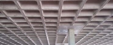 Vista inferior de laje nervurada em concreto armado, com nervuras aparentes apoiadas em pilares estruturais.