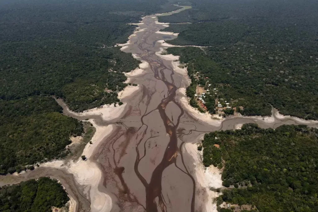 Seca extrema na Amazônia com rio quase seco, revelando leito arenoso e canais de água em meio à floresta