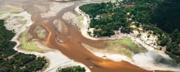 Rio da Amazônia com nível de água extremamente baixo, mostrando leito exposto, bancos de areia e floresta ao redor